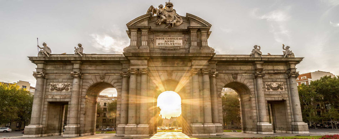 Puerta de Alcalá, surrounded by gardens and pierced by the evening sun.